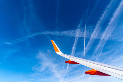 Wing of airplane flying against blue sky with contrails. traveling concept