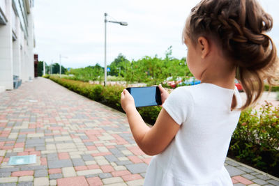 Girl photographing through smart phone against sky