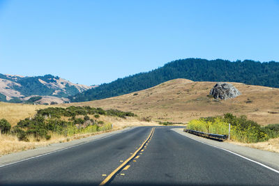 Road leading towards mountains against clear blue sky