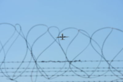 Close-up of barbed wire against sky seen through fence