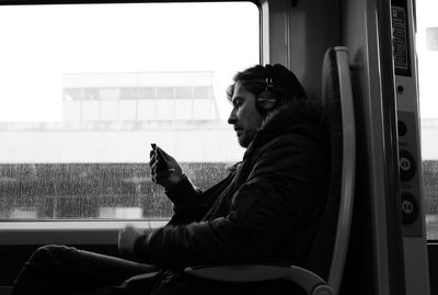 Side view of man using phone while sitting in bus