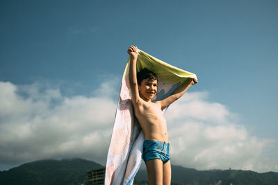 Boy on beach with towel flutters in wind like superman cape. happy child in summer against mountains