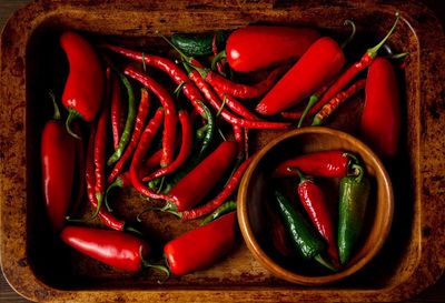 A scattering bunch of red chilies and green romano peppers on a wooden tray. 