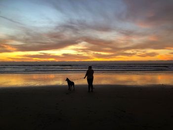 Silhouette men on beach against sky during sunset