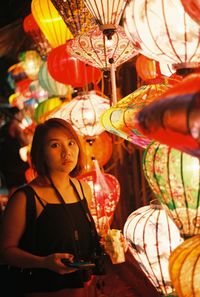 Portrait of young woman standing by illuminated lanterns