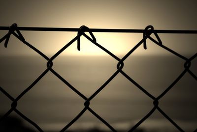 Close-up of chainlink fence against sea during sunset