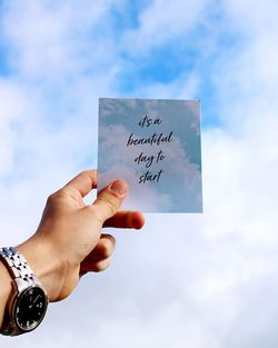 Cropped hand holding paper with text against sky