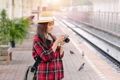 Woman holding umbrella while standing by railroad tracks