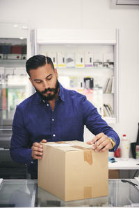 Male owner packing box at counter in electronics store