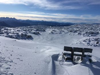 Scenic view of snowy landscape with a bench against mountain range in the dolomites during winter