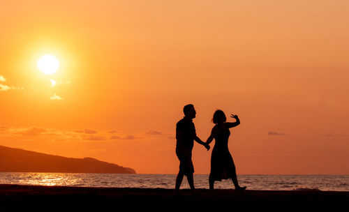Couple holding hands at beach, silhouette in sunset, love and friendship.
