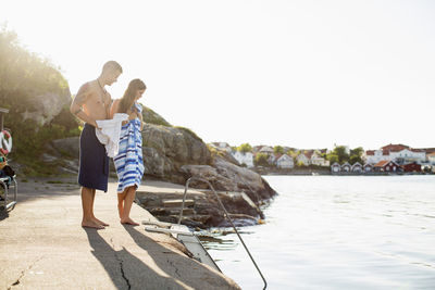 Full length of young couple wrapped in towel standing by lakeshore