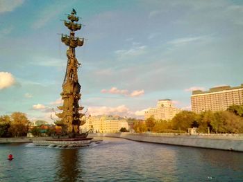 Statue by river against buildings in city against sky