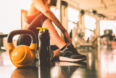 Low section of woman with kettlebell and water bottle sitting in gym