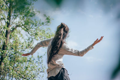 Low angle view of woman with arms outstretched against sky