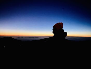 Silhouette man on rock against sky during sunset