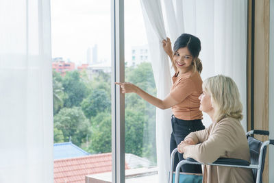 Young woman looking through window at home