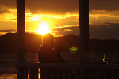 Silhouette woman sitting on mobile phone against sunset sky