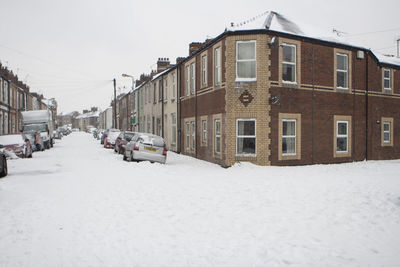 Snow covered street amidst houses in city