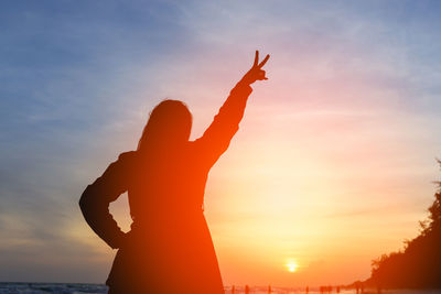 Silhouette person with arms raised against sky during sunset