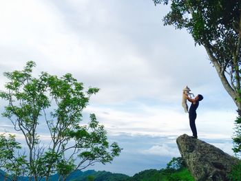 Full length of man holding dog while standing on rock against sky