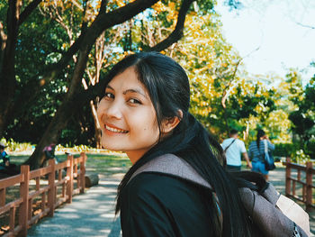 Portrait of young woman standing against trees