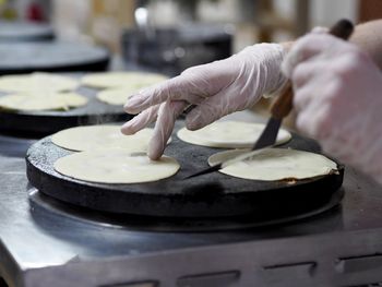 The guy cook in gloves pours a portion of batter with a ladle on an electric stove 