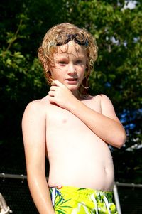 Low angle portrait of shirtless boy standing against trees