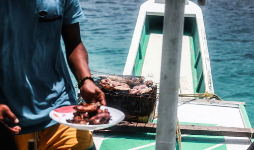 Midsection of man holding food plate while standing in boat sailing on sea