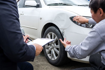 Midsection of client showing damage on car while insurance agent writing on clipboard