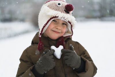 Child enjoying winter. the boy holds a heart made of snow in his hands in winter day. love concept.