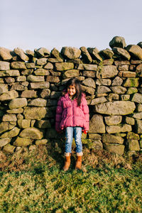 Full length of man standing on log stack against stone wall