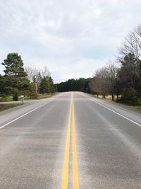 Empty road by trees against sky