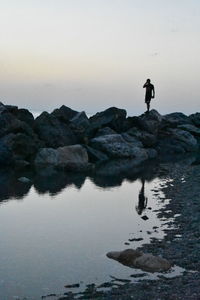 Silhouette people standing on rock by sea against sky