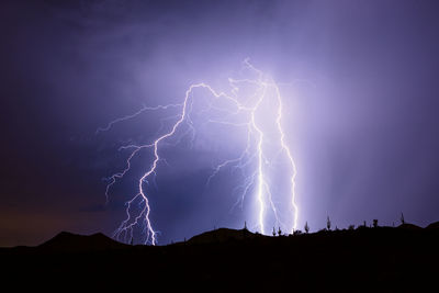 A lightning strike from a monsoon storm reveals saguaro cactus silhouettes in the arizona desert.