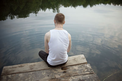 Rear view of man sitting on lake