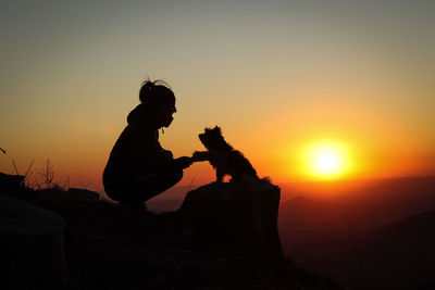 Silhouette woman sitting on rock against sky during sunset