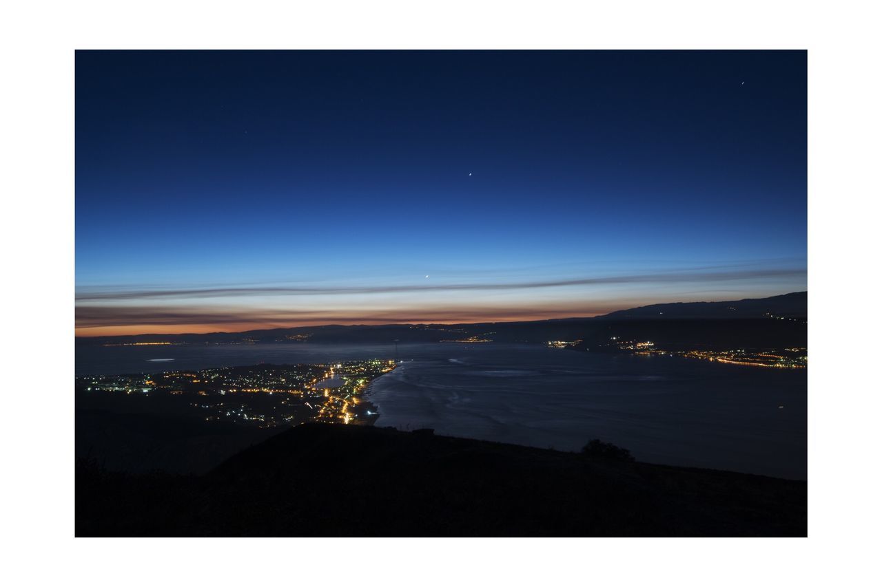 sea, water, illuminated, night, cityscape, scenics, transfer print, copy space, city, tranquil scene, sky, auto post production filter, mountain, beauty in nature, tranquility, coastline, building exterior, high angle view, clear sky, nature