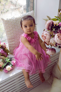 Girl child in pink dress sitting on the window on the white windowsill