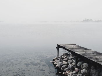 Pier by calm lake against sky during foggy weather