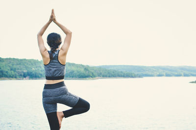 Rear view of woman practicing yoga at riverbank