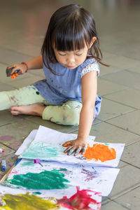 Full length of cute girl painting on paper while sitting on floor