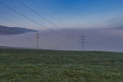 Electricity pylon on field against sky at dusk