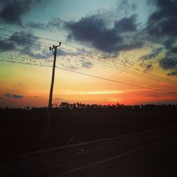 Low angle view of silhouette electricity pylon against dramatic sky