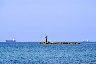 Lighthouse by sea against clear sky