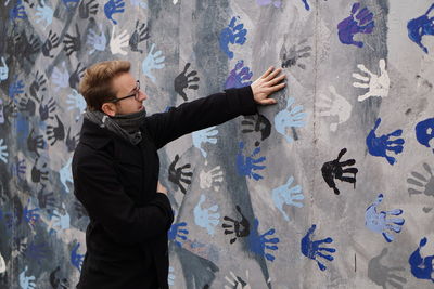 Young man standing by wall with hand prints
