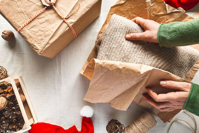 Woman's hands wrapping woolen sweater in craft recycled paper on the table with christmas decoration