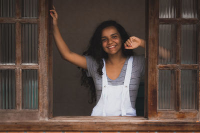 Portrait of smiling young woman standing against wooden wall