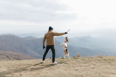 Rear view of man playing with dog while standing on mountain