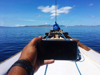 Midsection of person holding sailboat in sea against sky